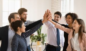 a group of people all slap hands in the middle of a meeting room