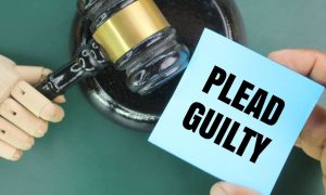 a robotic hand holding a gavel while a human hand holds a plead guilty note